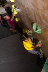 bouldering, little girl climbing up the wall and climber multicolored grips. Leisure activity