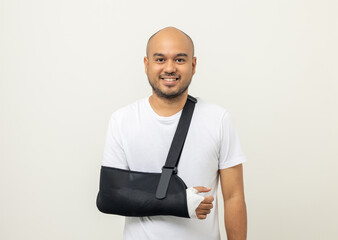 Happy young asian man broken arm on isolated background. Asian man put on plaster bandage cast...