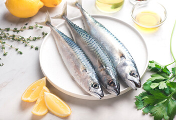 Fresh mackerel with recipe ingredients: olive oil, sea salt, parsley, lemon, herbs. White marble table, front view