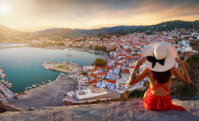 A tourist woman with hat sits high above the town of Skopelos island and enjoys the beautiful...