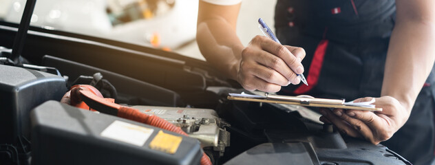 Auto check up and car service shop concept. Mechanic writing job checklist to clipboard to estimate repair quotation to client at workshop garage. - obrazy, fototapety, plakaty