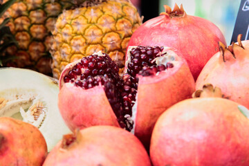 Red pomegranate fruit on a market stall with a blurred ananas on the background. Selective focus
