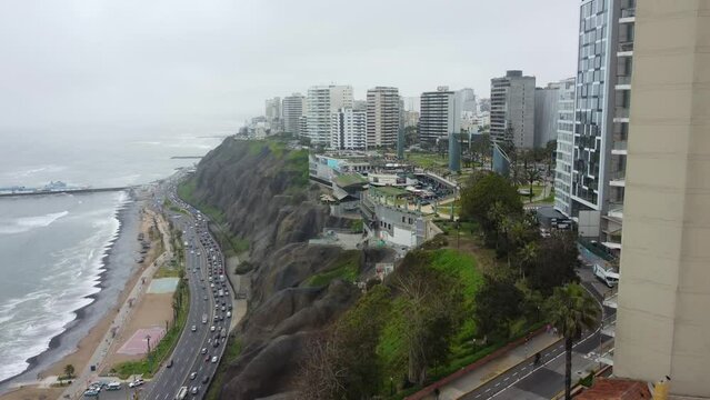 Drone 4k video of a shopping center called "Larcomar" on the edge of the coast of Lima, Peru in the Miraflores district. To the left below is the pacific ocean and freeway. Drone flies slowly forward.