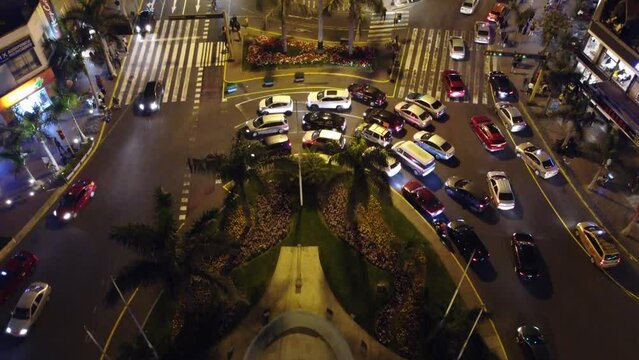 4k Drone video of night time Lima, Peru. Recorded in "Parque Kennedy" or Kennedy Park in the Miraflores district. Drone hovers above round about and camera tilts up. Many cars in traffic on the street
