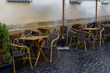 Empty wet wooden table and chairs on terrace of outdoor cafeteria during rain. Street city life in rain