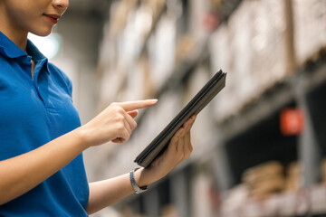 Young female worker in blue uniform checklist manage parcel box product in warehouse. Asian woman employee holding tablet working at store industry. Logistic import export concept.