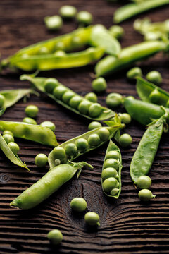 Green peas in split pods on a wooden background, close up view