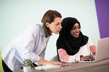 Afro woman with a hijab and a European woman using a smartphone and laptop in their home office