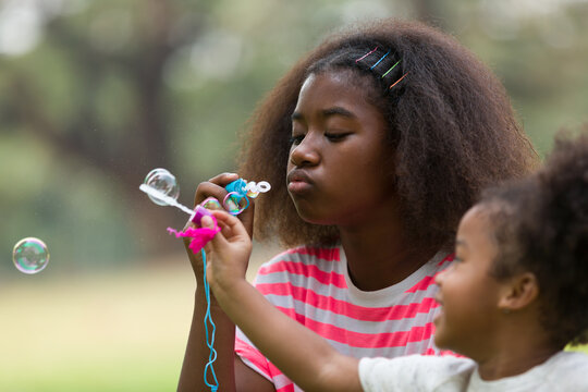 Two African American children playing and blowing soap bubbles outdoor in the park. Group of child girl having fun with blowing soap bubbles together outside