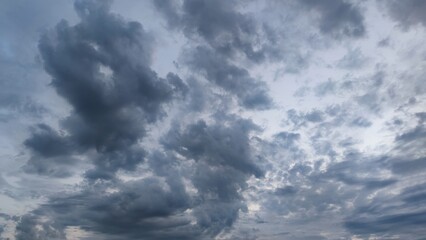 Cloudy sky with stormy clouds. Low cumulus clouds of various shapes cover almost the entire sky. They are at different heights and have different colors of white, light gray and dark blue.