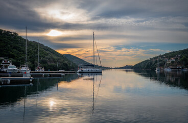 Sunrise in Sivota bay, Lefkada island, Greece with cloudy sky and golden light casting reflections on the calm water.
