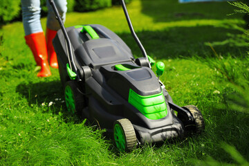 Woman cutting grass with lawn mower in garden on sunny day, closeup