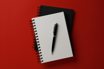 Notebooks and pen on red background, top view