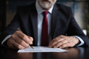 Businessman signs documents with a pen making the signature sitting at the desk.