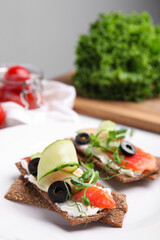 Tasty rye crispbreads with salmon, cream cheese and vegetables on plate, closeup