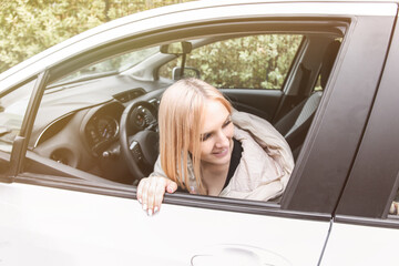 A young blonde looks out of the car window and smiles. Acquaintance on the road