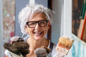 smiling happy older woman portrait, proud artist, in her fifties with grey hair and black glasses...