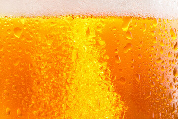 Glass of tasty cold beer with foam and condensation drops as background, closeup