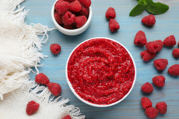 Raspberry puree in bowl and fresh berries on light blue wooden table, flat lay