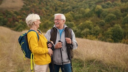Active senior couple with backpacks hiking together in nature on autumn day. - Powered by Adobe