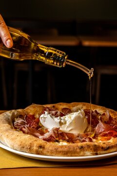 Vertical Of A Person Pouring Olive Oil On A Pizza With Mozzarella Baked In The Wood Oven.