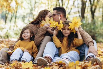 Family with two daughters sitting in park in autumn leaves