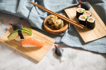 Fototapeta Lachs Avocado Sushi als Nigiri, Maki, roh und knusprig frittiert auf Holz Teller mit Soja Soße in Fisch Verpackung und Stäbchen auf Stein Hintergrund hell obraz