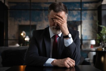 Frustrated mature man sitting in a modern office. Overworked businessman with terrible migraine