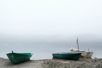 Naklejka na ściany i meble Wooden boats on shore of lake in calm misty day. 