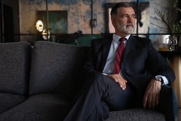 Starting new working day. Mature businessman sitting on the couch in office.