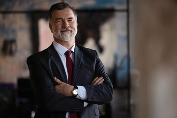 Confident mature business man with arms crossed looking at camera, smiling standing in modern office