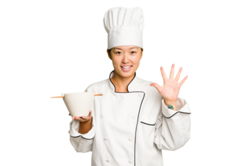 Young chef asian woman holding a bowl of ramen isolated smiling cheerful showing number five with fingers.