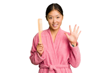 Young asian woman holding an hair comb isolated smiling cheerful showing number five with fingers.