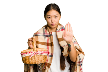 Young asian woman holding a picnic basket isolated standing with outstretched hand showing stop sign, preventing you.