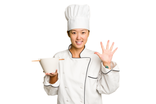 Young chef asian woman holding a bowl of ramen isolated smiling cheerful showing number five with fingers.