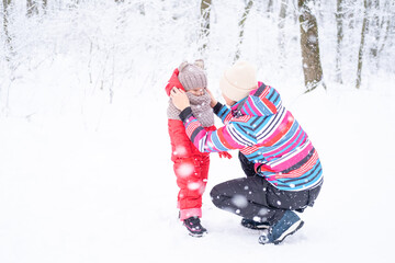 Fototapeta na wymiar Mother and daughter in colorful clothes having fun on winter walk in nature