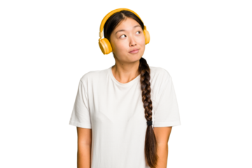 Young asian woman listening to music with headphones isolated dreaming of achieving goals and purposes