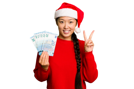 Young asian woman celebrating Christmas holding banknotes isolated showing number two with fingers.