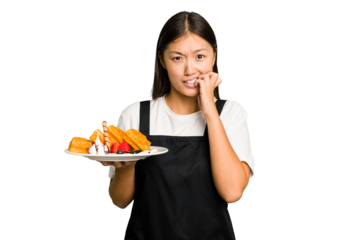 Young asian waitress woman holding waffles isolated biting fingernails, nervous and very anxious.