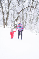 Mother and daughter in colorful clothes having fun on winter walk in nature