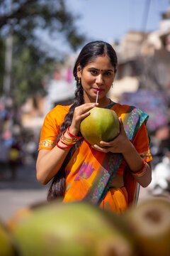 Portrait of young woman drinking green coconut water on street