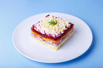 Herring salad under a fur coat. Traditional Russian multilayered salad from herring, beets, potatoes, carrots and eggs. Close-up, blue background.