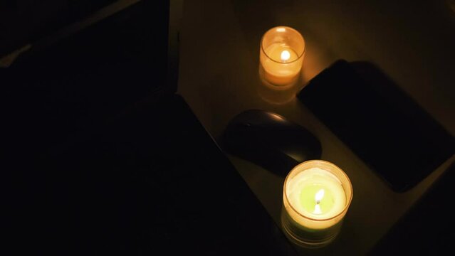 Burning candles, laptop and cellphone on the table. Candles in dark room. No electricity in the house. Power outage in the city. Blackout, energy crisis concept. 