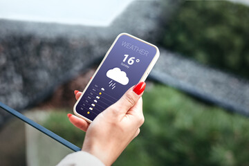 rainy weather forecast. female hand holds a mobile phone and looks at the weather forecast for the...