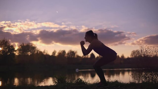 Silhouette of A young girl doing squats at the morning. Fitness training outside the gym, outdoor workout.
