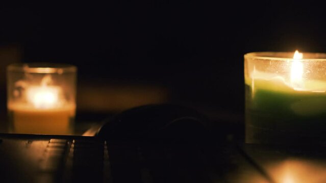 Burning candles, laptop and cellphone on the table. Candles in dark room. No electricity in the house. Power outage in the city. Blackout, energy crisis concept. 