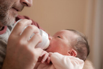 lifestyle portrait of proud happy man holding tenderly bottle feeding her child - an adorable and beautiful newborn baby girl in father and daughter love and bonding concept