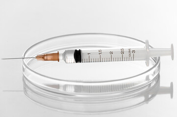 Syringe and needle with liquid transparent vaccine for injection on petri dish in laboratory white...
