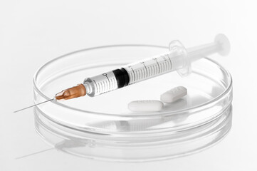 Syringe with liquid transparent vaccine for injection and white pills on petri dish in laboratory...