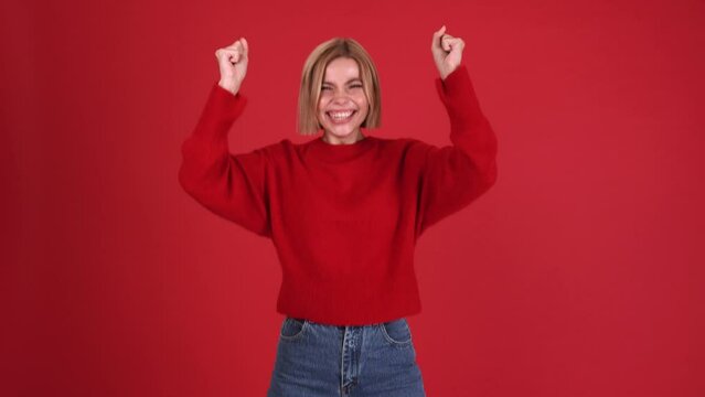 Worried blonde woman wearing red sweater rejoicing at the camera in the red studio